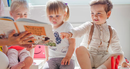 Drei Kleinkinder schauen sich gemeinsam ein Buch an