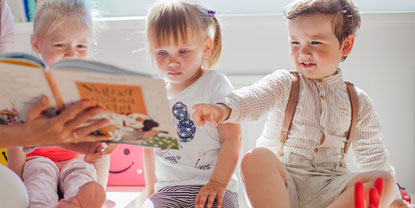 Drei Kleinkinder schauen sich gemeinsam ein Buch an